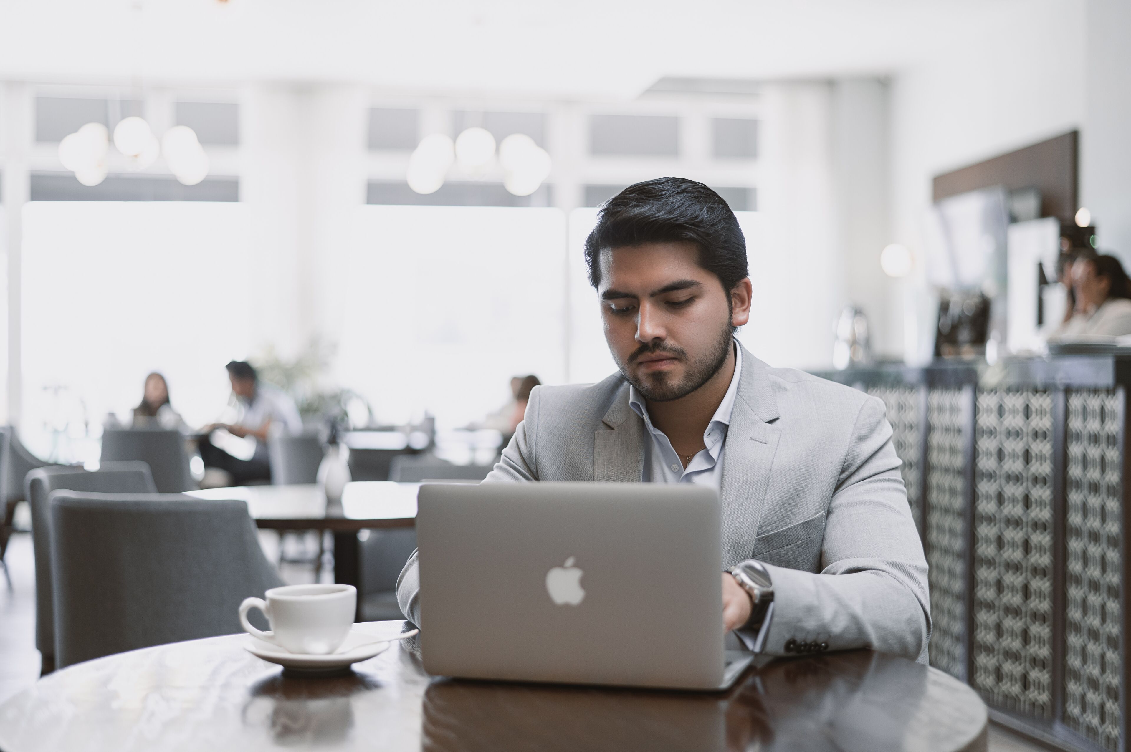 A person using a laptop at a table in a modern cafe with a cup on the table.