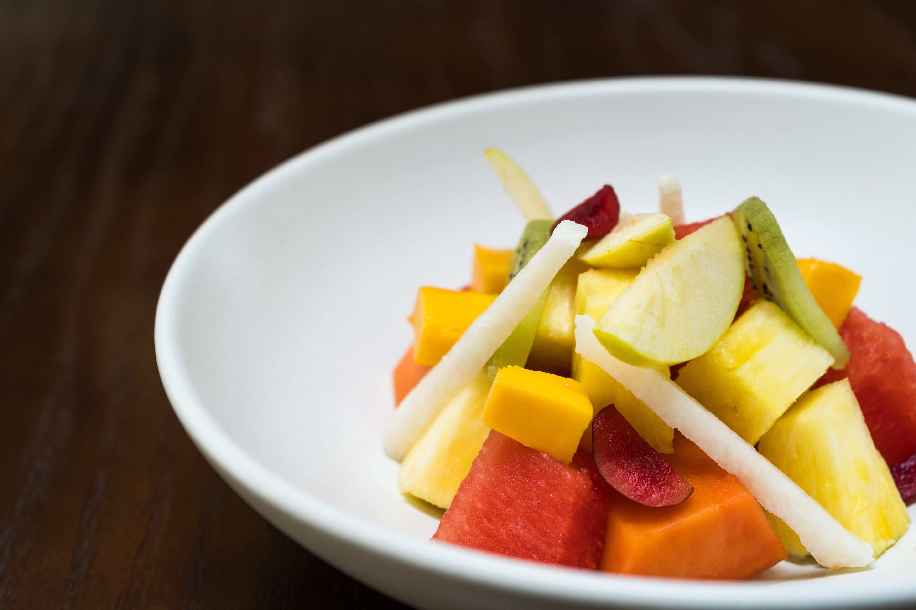 A white bowl filled with a variety of fruits including watermelon, pineapple, and mango.