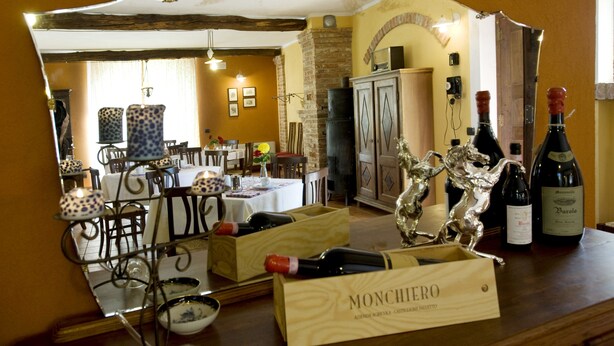 A dining area with a table set for two, a wine rack with bottles, and a mirror reflecting the room. - Agriturismo Cascina Monchiero (Bra)