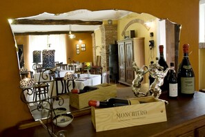 A dining area with a table set for two, a wine rack with bottles, and a mirror reflecting the room. - Agriturismo Cascina Monchiero (Bra)
