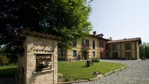 A traditional stone building with a small garden area, a gravel driveway, and a large tree providing shade. - Agriturismo Cascina Monchiero (Bra)