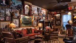 Une pièce chaleureuse avec un canapé rouge, des chaises en bois, une table d’échecs et divers tableaux encadrés accrochés aux murs.