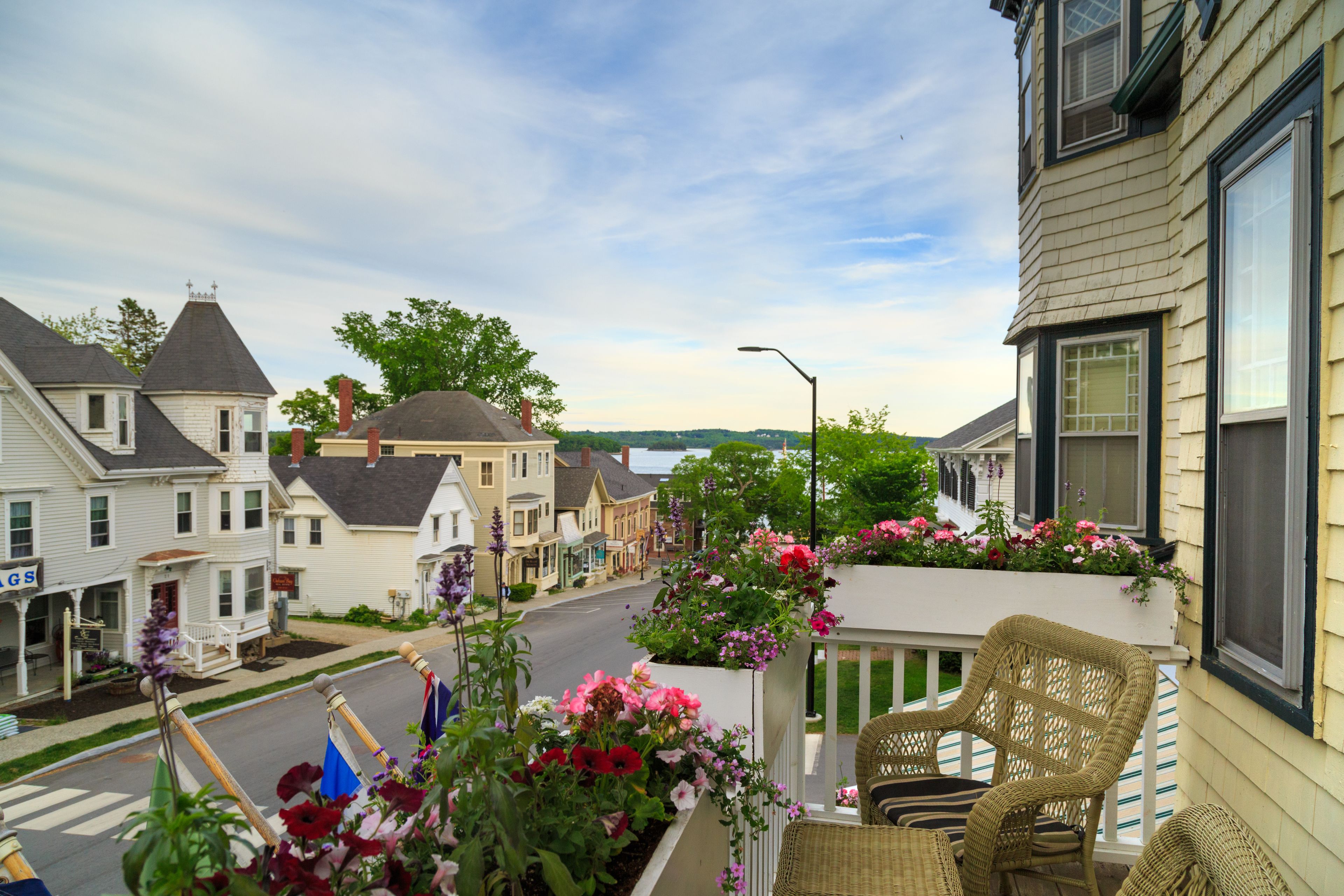 A residential street with houses, a balcony with wicker furniture, and flower boxes.