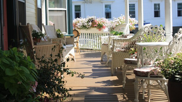 Une terrasse en bois, meublée de meubles en osier, et entourée d’une clôture en bois peinte en blanc.