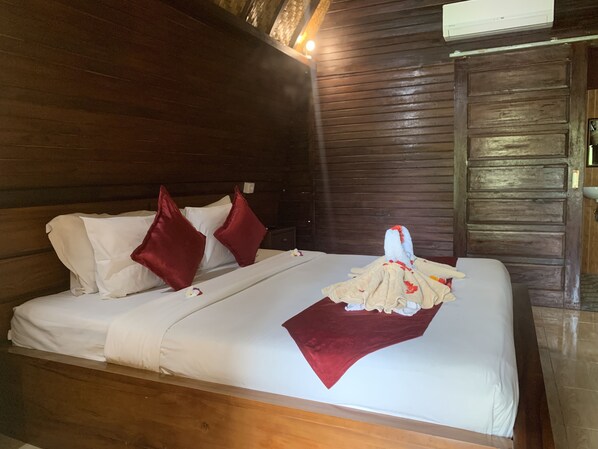 A wooden cabin-style room with a bed, red pillows, and a blanket. - Jona Bungalow (Penida Island)