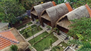 A traditional thatched-roof building with a tiled roof, surrounded by a well-maintained garden with palm trees and a patterned walkway. - Jona Bungalow (Penida Island)