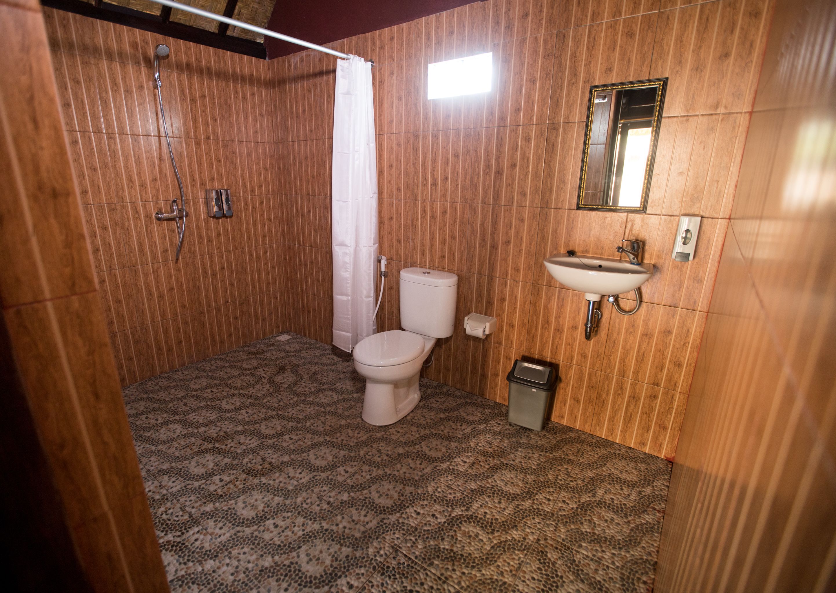 Un baño con paredes de paneles de madera, una ducha, un inodoro, un lavabo y un espejo.