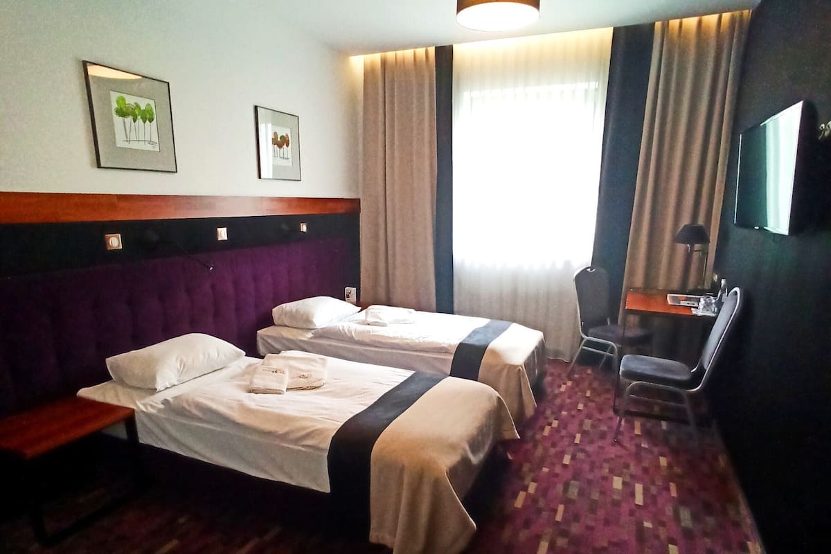 A hotel room with two beds, a desk, a chair, a TV, and a window with curtains.