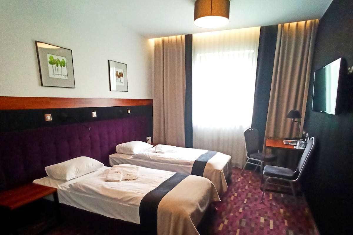 A hotel room with two beds, a desk, a chair, a TV, and a window with curtains.