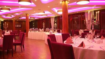 Une salle de banquet avec des tables rondes, des chaises rouges et des nappes blanches.