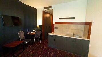 Une chambre d’hôtel compacte comprenant un coin cuisine, un petit espace repas avec une table et deux chaises, et un téléviseur fixé au mur.
