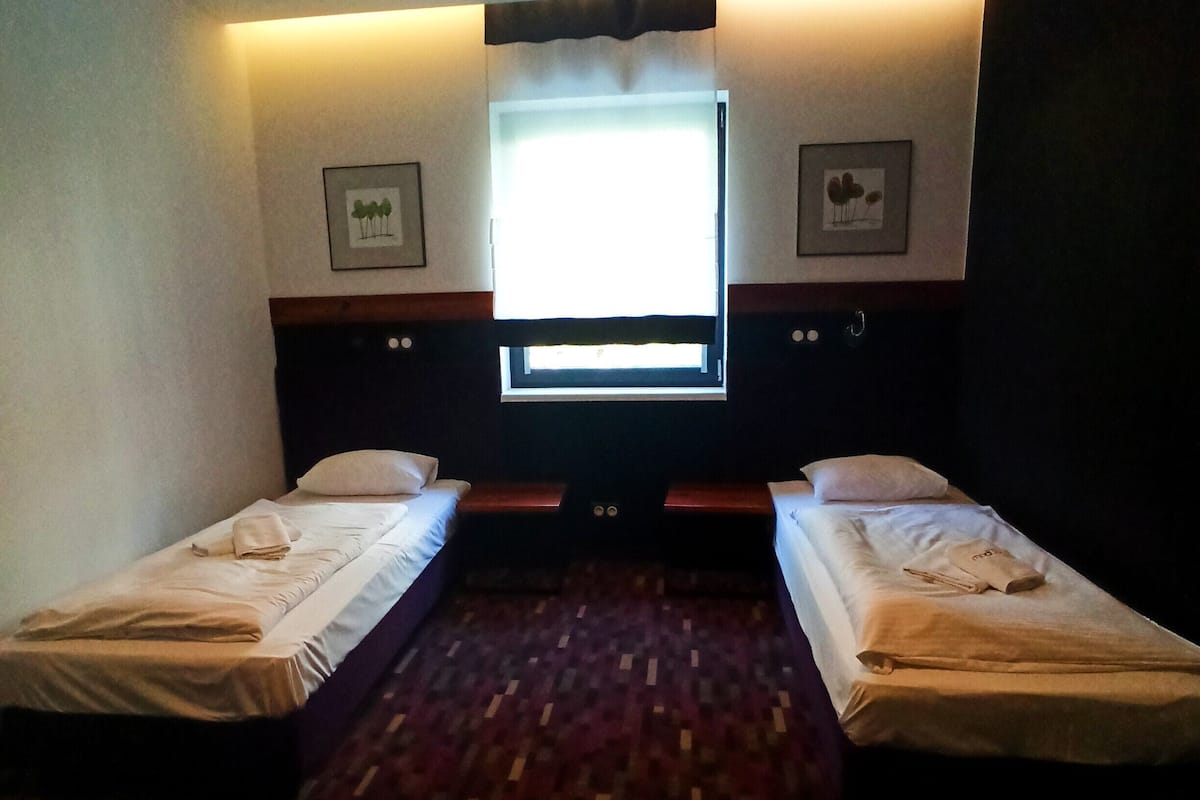 A hotel room with two single beds, a large window, and a flat-screen TV.