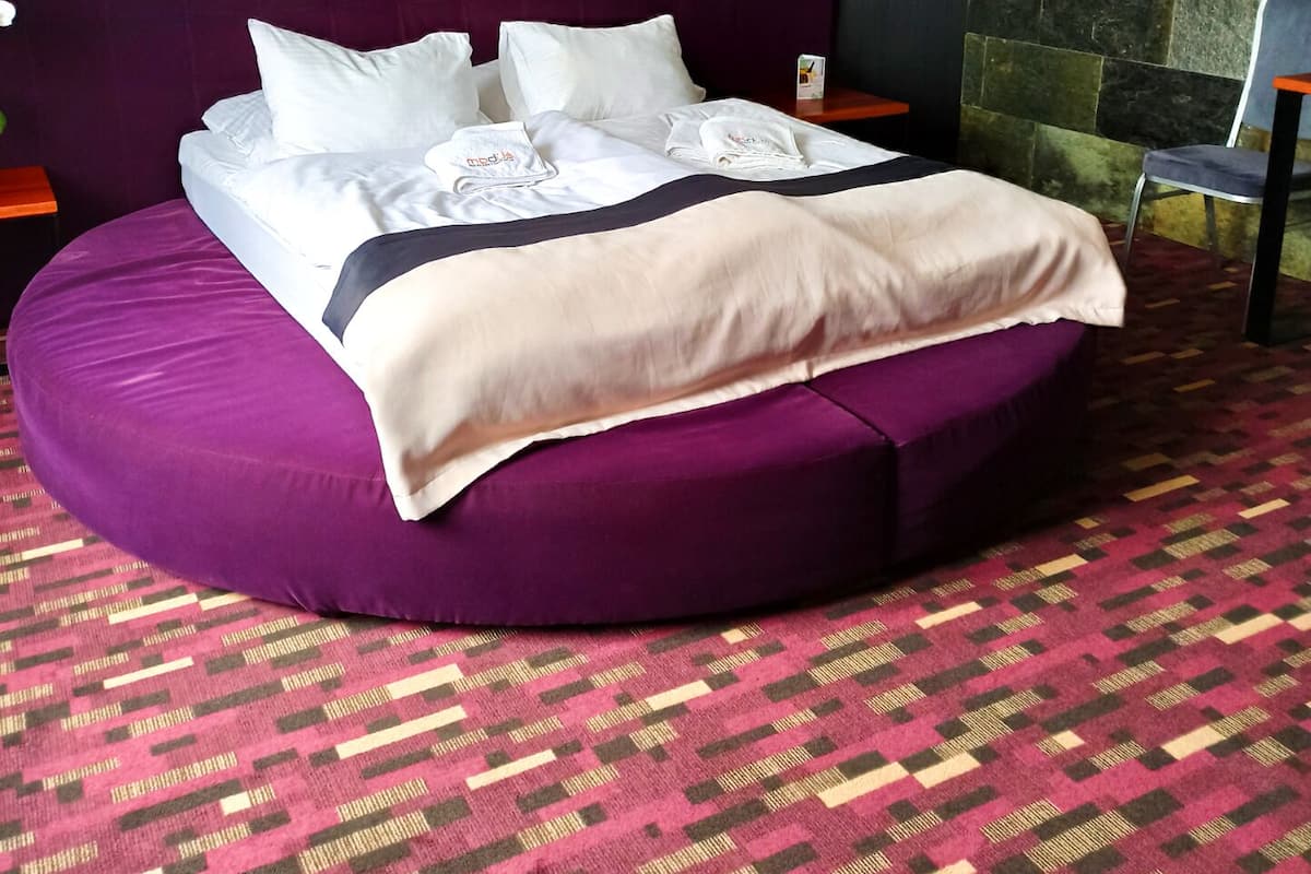 A circular bed with a purple headboard, white bedding, and a patterned carpet.