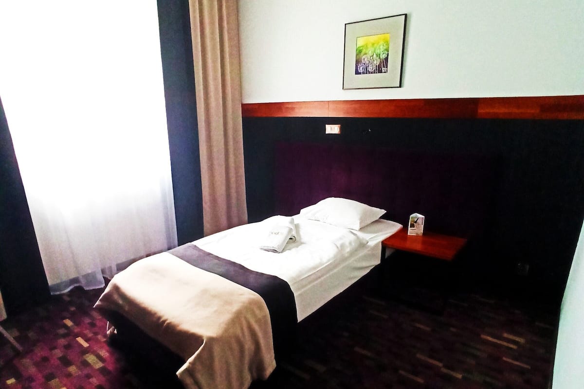 A hotel room with a bed, a nightstand, a framed picture on the wall, and a patterned carpet.