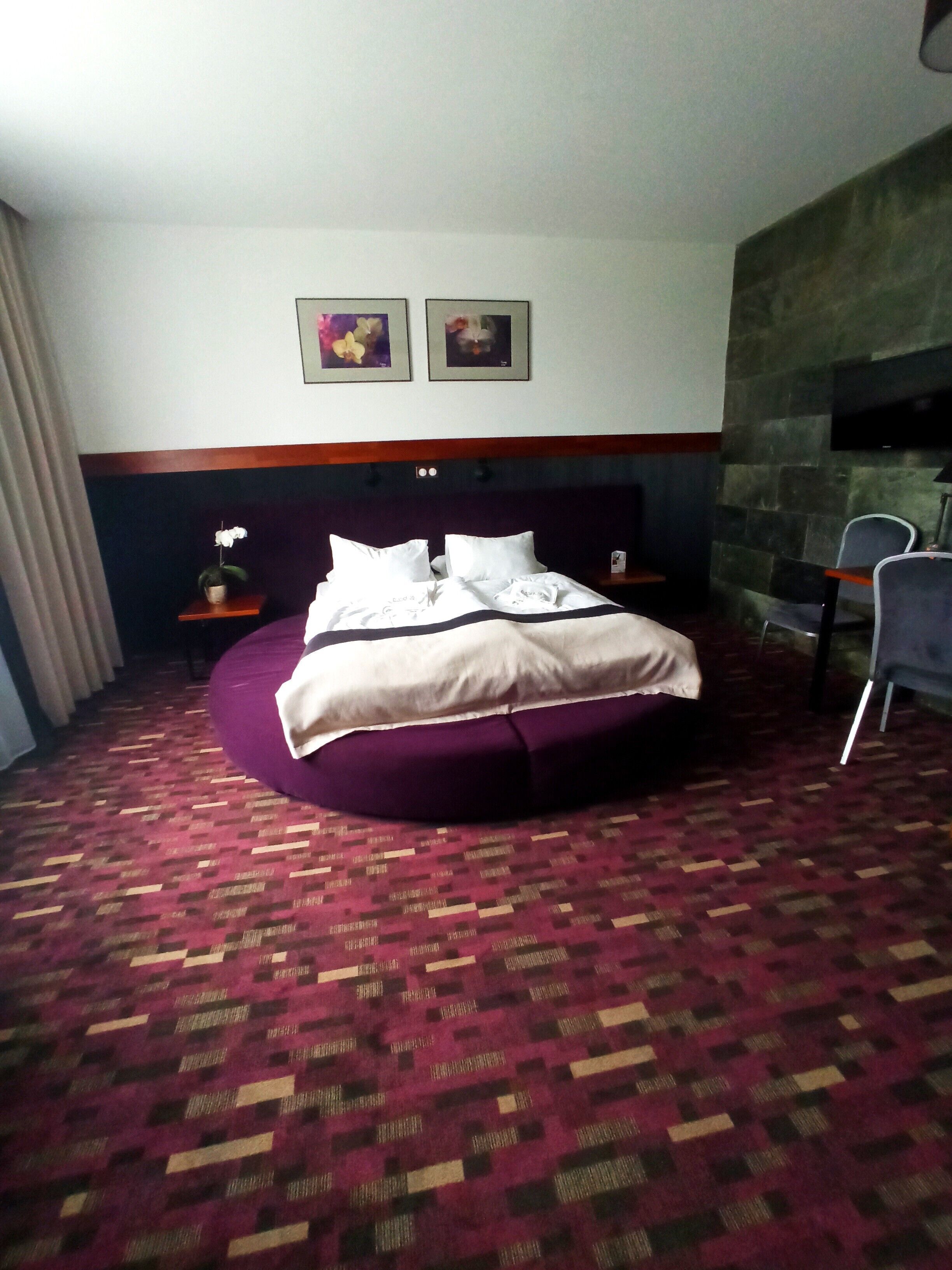 Una camera d'albergo con un letto rotondo, un camino in pietra e un tavolino con una lampada.