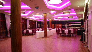 Un amplio salón de banquetes con mesas y sillas redondas, columnas de madera e iluminación de techo moderna.