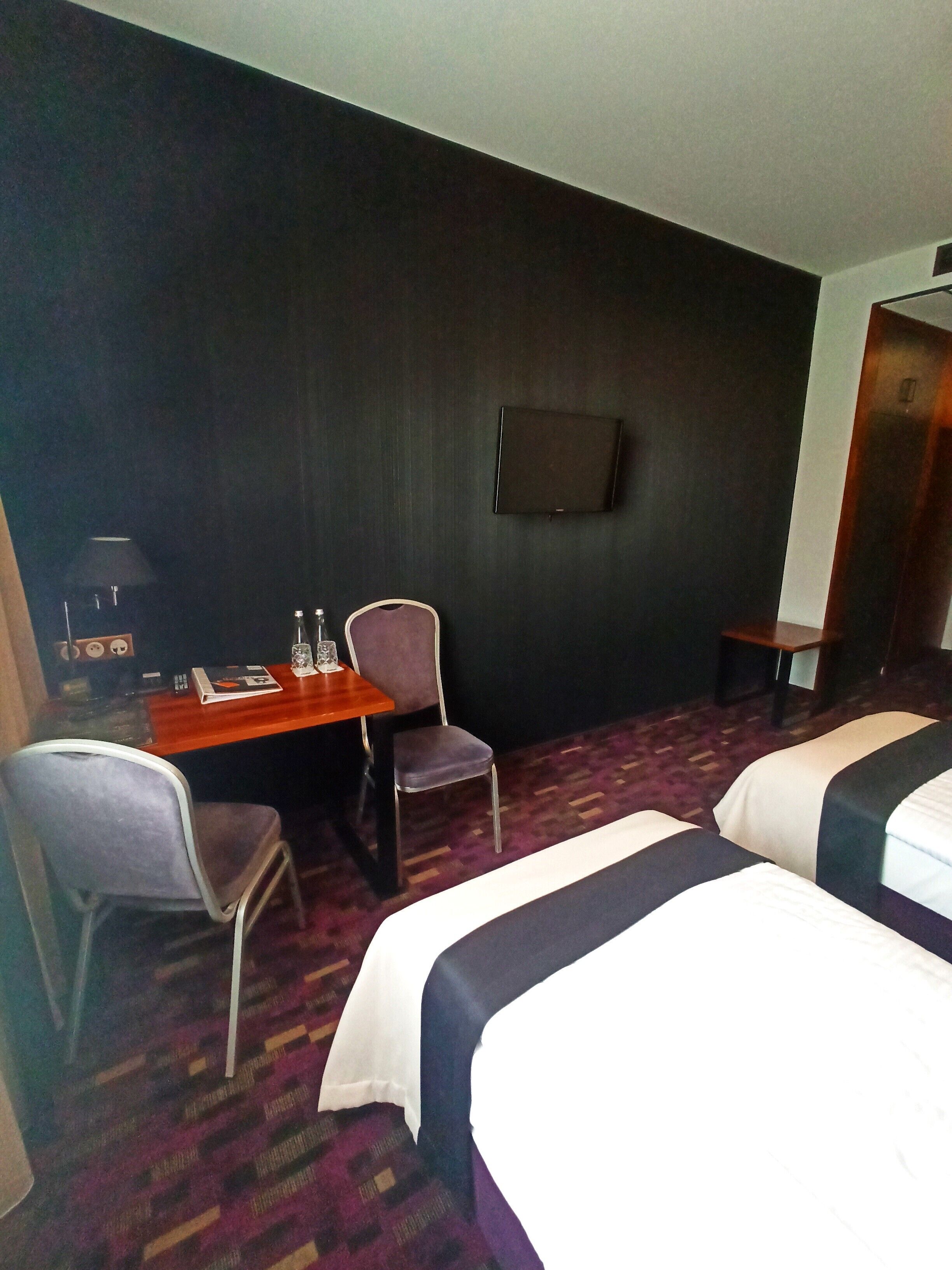 Una habitación de hotel con escritorio, dos sillas, una cama y televisión en la pared.