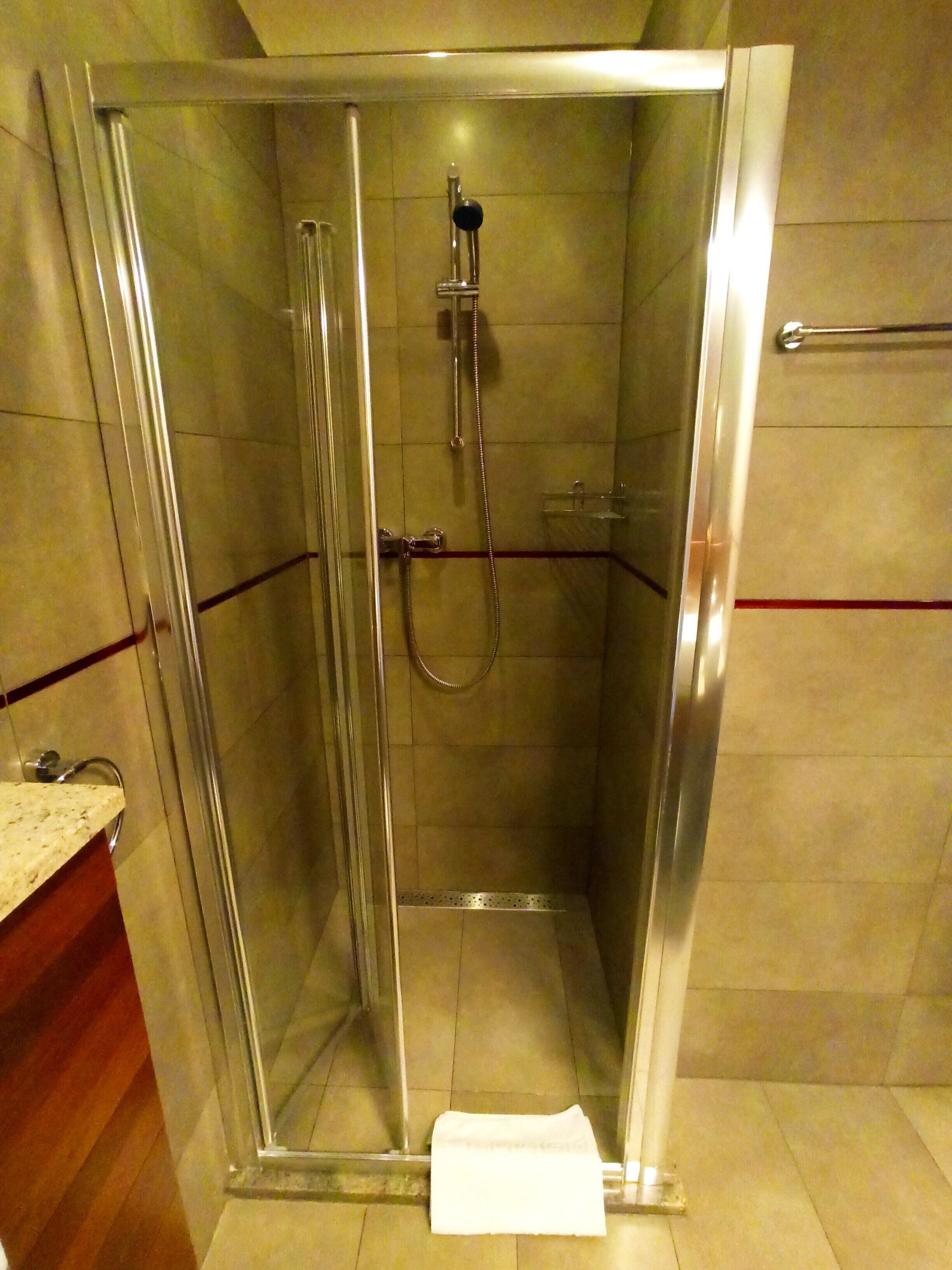 A glass-enclosed shower stall with a handheld showerhead and a handheld shower attachment.