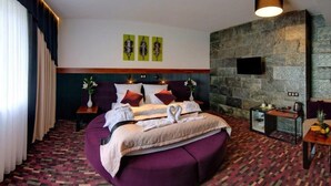 Una habitación de hotel moderna con una cama grande, una pared decorativa de piedra, un televisor de pantalla plana y una pequeña mesa con frutero.