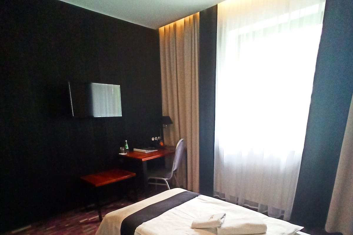 A hotel room with a bed, a desk, a chair, a television, and a window with curtains.
