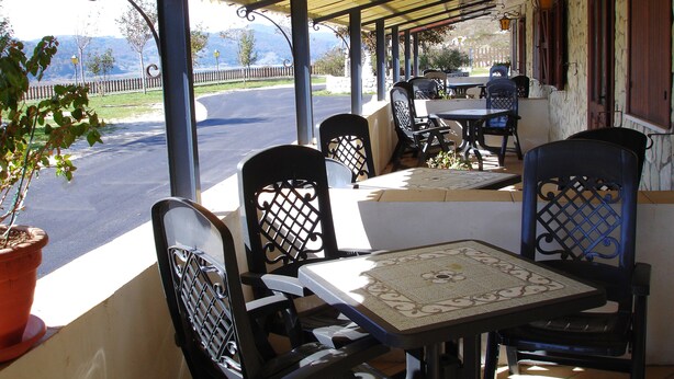 A covered outdoor seating area with tables and chairs, a potted plant, and a view of the street and mountains. - Agriturismo Falode (Castello del Matese)