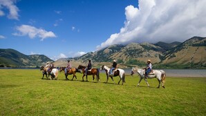 A group of people riding horses across a grassy field with mountains in the background. - Agriturismo Falode (Castello del Matese)
