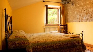 A bedroom with two beds, a stone wall, a window with curtains, and a television mounted on the wall. - Agriturismo Falode (Castello del Matese)