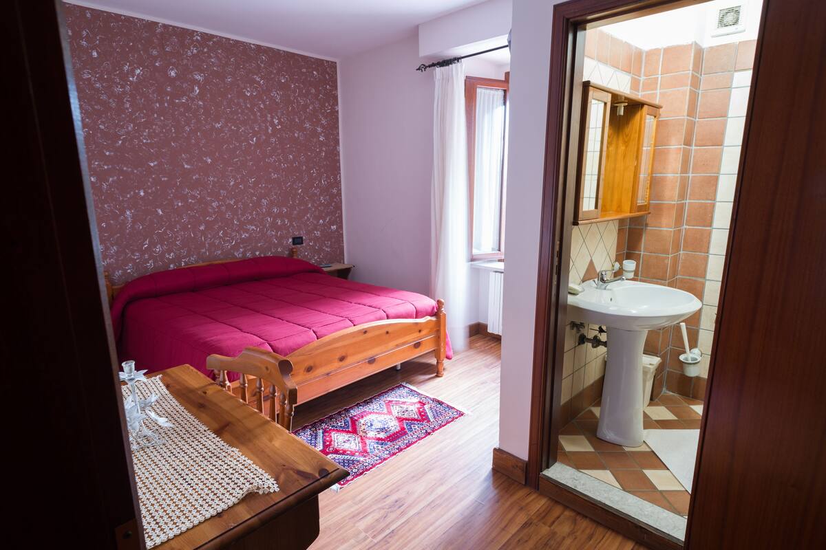 A bedroom with a wooden bed, a bedside table, and a window with curtains.