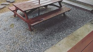 A wooden picnic table with a green umbrella, surrounded by gravel and greenery. - Kawaraya-Ikinpata (Motobu)
