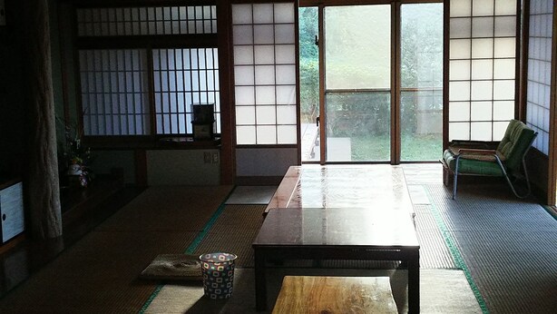 A traditional Japanese room with tatami flooring, a wooden table, sliding doors, and a view of greenery outside. - Kawaraya-Ikinpata (Motobu)