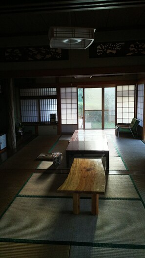 A traditional Japanese room with tatami flooring, a wooden table, sliding doors, and a view of greenery outside. - Kawaraya-Ikinpata (Motobu)