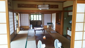 A traditional Japanese room with tatami flooring, a low table, a chair, a fan, and a sliding door. - Kawaraya-Ikinpata (Motobu)