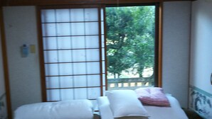 A traditional Japanese room with tatami flooring, a low bed with a pillow, a futon, and a sliding shoji screen door. - Kawaraya-Ikinpata (Motobu)