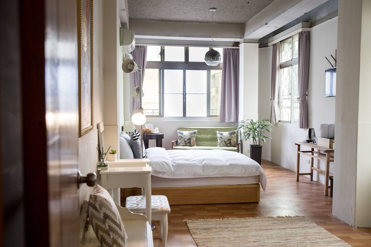A bedroom with a bed, bedside table, lamp, and a window with curtains.
