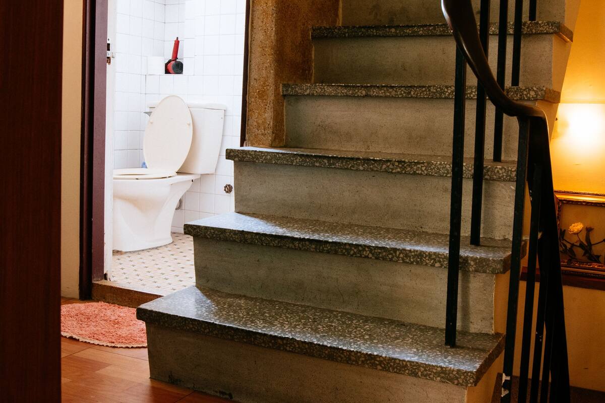 A staircase with a handrail leading to a bathroom with a toilet and a shower.