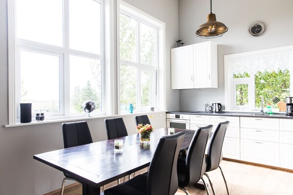 Une cuisine moderne avec des meubles blancs, une table à manger en bois foncé et une grande fenêtre donnant sur les arbres.