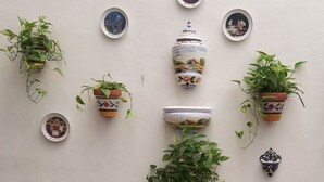 Un patio con sillas de mimbre, una mesita pequeña y varias macetas con plantas, además de platos decorativos en la pared.
