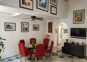 A dining area with a round table, red upholstered chairs, a ceiling fan, and framed artwork on the walls.