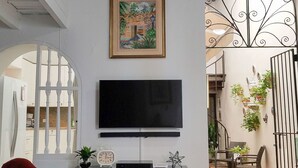 Una sala de estar con un televisor sobre un mueble negro, un cuadro enmarcado encima y un sillón rojo.