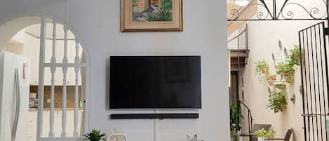 A living room with a TV on a black cabinet, a framed painting above it, and a red chair.