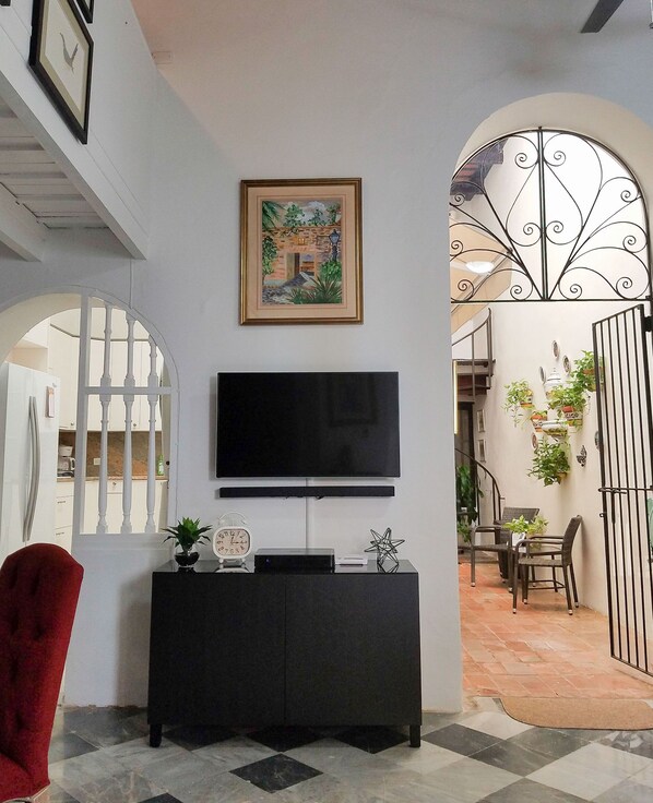 A living room with a TV on a black cabinet, a framed painting above it, and a red chair.