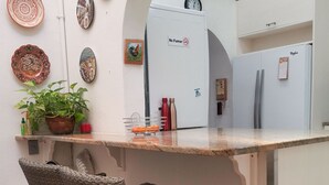 Una cocina compacta con un refrigerador blanco, una pequeña isla con un lavamanos y sillas de mimbre.