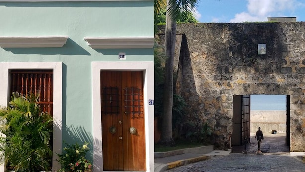 Un edificio con fachada verde, una puerta de madera y un muro de piedra con un portón.