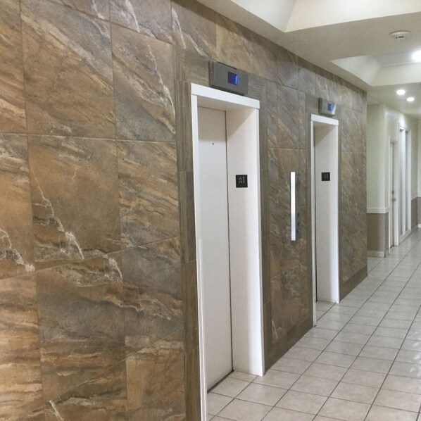 A hallway with marble walls and tiled flooring, featuring three elevators with visible floor numbers.