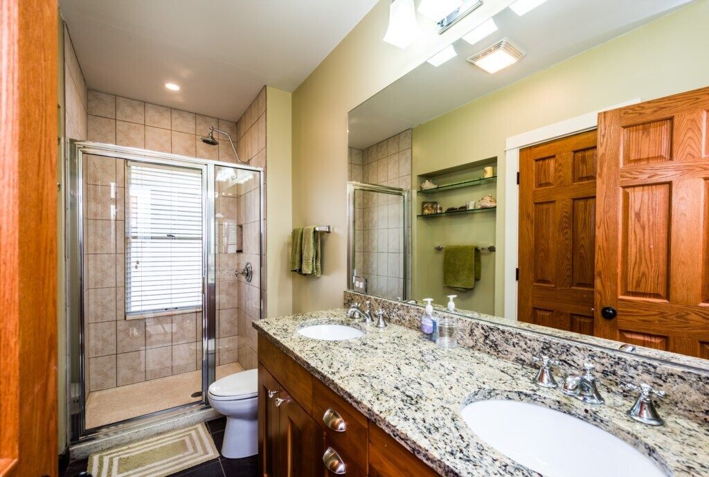 A bathroom with a glass shower enclosure, a double sink vanity, and a large mirror.
