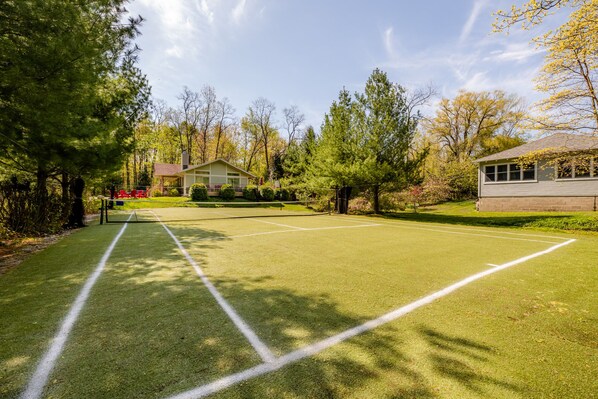 A tennis court with a net, surrounded by trees and a building.