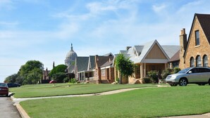 Una calle residencial con casas, césped y un automóvil.