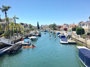 Un port de plaisance avec des bateaux amarrés le long de la rive, un pont piétonnier et des maisons en arrière-plan.