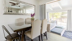 A room with a dining table, chairs, a ceiling fan, a large mirror, and a view of the outdoors through a window with curtains. - Naples Island Pool House (Long Beach)
