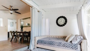 A bedroom with a bunk bed, a ceiling fan, a clock, and a dining area with chairs and a table. - Naples Island Pool House (Long Beach)